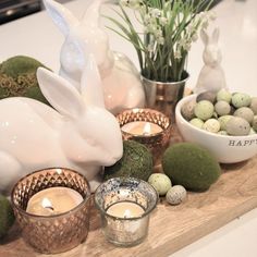 a wooden tray topped with candles and bunny figurines next to bowls filled with eggs