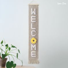 a wall hanging with the word home and a sunflower on it next to a potted plant