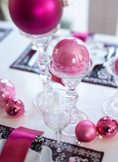 two wine glasses are sitting on a table with pink ornaments around the glass and ribbon