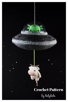 a stuffed animal hanging from a string in the shape of an alien ship on a black background