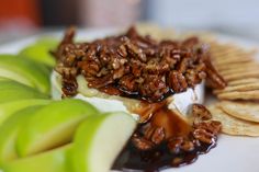 a white plate topped with crackers, apples and cheese covered in pecanse