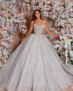 a woman standing in front of a floral backdrop wearing a wedding dress with beading