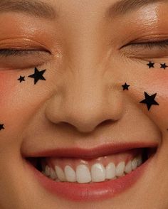 a smiling woman with stars painted on her face and eyebrows, looking at the camera