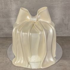 a white cake with a large bow on it's top sitting on a plate