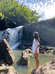 a girl standing on rocks in front of a waterfall