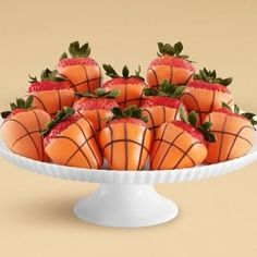 strawberries are arranged in the shape of basketballs on a white platter with green leaves