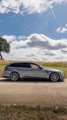 a silver car parked on the side of a road next to a tree and grass