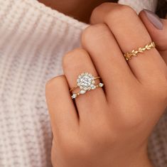 a woman's hand wearing a gold ring with a diamond center and leaves on the band