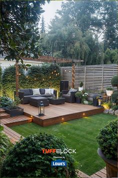 an outdoor living area with wooden decking and lights on the grass, surrounded by trees