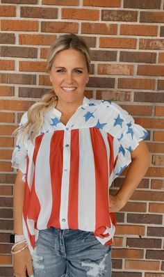 a woman standing in front of a brick wall wearing an american flag shirt and ripped jeans