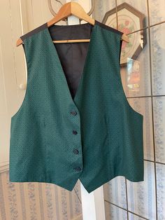 This tailored vest is made from a polyester blend in a beautiful shade of dark emerald green with a pattern (see the close-up for the pattern, not the colour!). It has the original buttons in the front, and the back and lining are made from black silky fabric. The measurements, taken with the vest lying flat, are: shoulder to shoulder, 16 inches; armpit to armpit, 25 inches; length, 26 inches in front and 24 inches in back; bottom edge, 25 inches. In very good condition. Classic Green Vest For Winter, Classic Green Winter Vest, Green Sleeveless Vest Outerwear, Fitted Green Vest Outerwear, Green Fitted Classic Vest, Winter Workwear Green Vest, Green Winter Workwear Vest, Elegant Green Vest For Formal Occasions, Elegant Fitted Green Vest