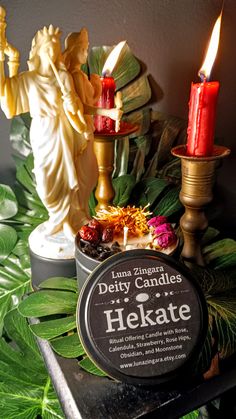 candles and other items on a table with green leaves in the background, including an angel statue