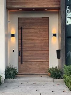 the front door to a modern home with lights on and plants in pots next to it