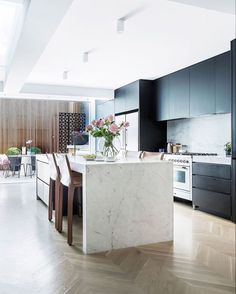 a kitchen with black cabinets and white marble counter tops, along with wooden flooring