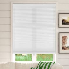 a living room with white walls and windows covered in cellular shades, green striped throw pillows