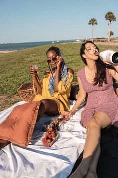 two women sitting on a blanket drinking wine