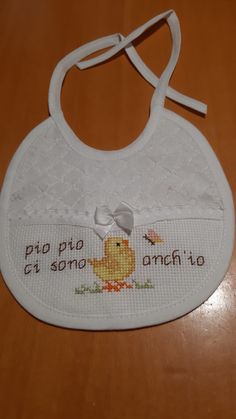 a white bib with an embroidered ducky on the front and words written in spanish