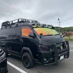 a black vehicle parked in a parking lot next to another car with an orange and yellow paint job on it