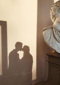 the shadow of two people kissing in front of a bust of a man and woman