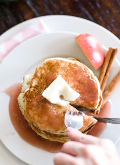 a person is cutting into some pancakes with butter and cinnamon on the side while holding a knife and fork