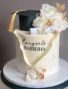 a graduation cake decorated with white flowers and black mortar on top, topped with a gold tassel