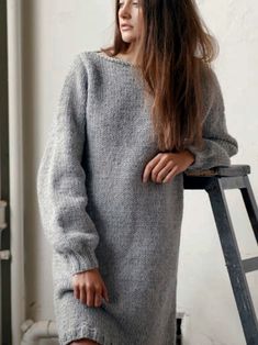 a woman standing in front of a window wearing a gray sweater dress with long sleeves