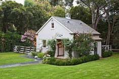 a small white house surrounded by lush green grass and flowers in the front yard area