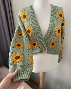 a woman is holding up a green crocheted sweater with sunflowers on it