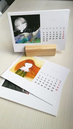 two calendars and a stamp sitting on a table next to each other in front of a photo