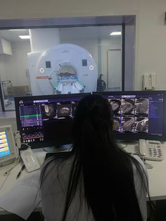 a woman sitting at a desk in front of two computer monitors with mri images on them