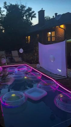 an outdoor pool is lit up with purple lights and floating bowls in the foreground