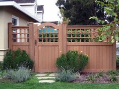 a wooden fence in front of a house with green grass and flowers on the side