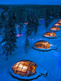 igloose cabins in the snow at night with lights shining on them, surrounded by trees