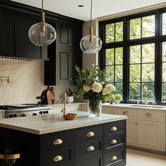 a kitchen with black cabinets and marble counter tops, two hanging lights above the island