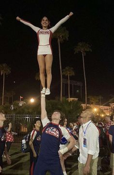 a cheerleader standing on top of another cheerleader in front of a crowd at night