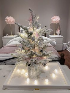 a white christmas tree with pink lights in a silver tinsel pot on a table