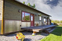 a small wooden cabin with a deck and picnic table in the front yard on a sunny day