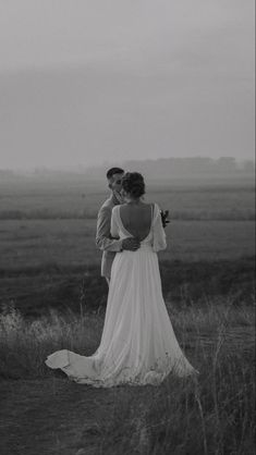 a bride and groom standing in the middle of a field with foggy skies behind them