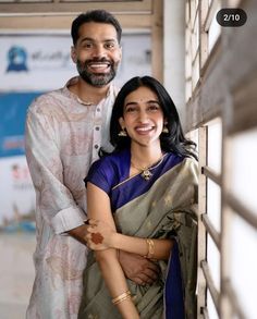 a man and woman standing next to each other in front of a window smiling at the camera