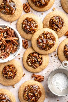 several pecan cookies are arranged on a table with one cookie broken in half and the other topped with pecans