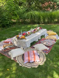 a table with pillows, candles and flowers on it in the middle of some grass