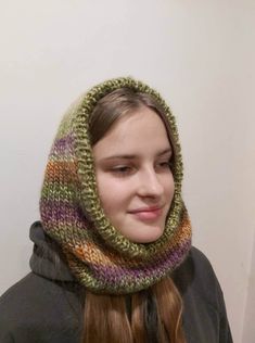 a young woman wearing a knitted cowl in front of a white wall