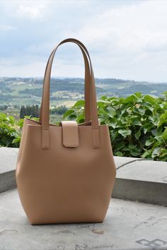 tan leather tote bag with tuscan hills in the background Bucket Tote Bag, Bucket Tote, Brown Tote, Everyday Accessories, Shopper Tote, Zip Pouch, Tuscany, Bucket Bag, In Italy