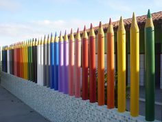 a row of colorful crayons sitting on top of a white fence next to a building