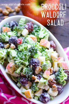 broccoli salad in a white bowl on a pink and white towel with an apple