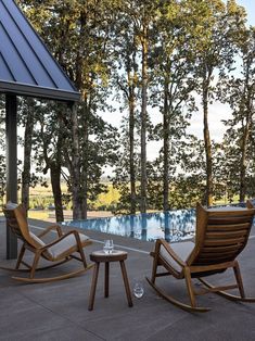 two wooden rocking chairs sitting next to a pool in the middle of a wooded area