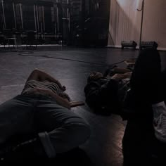 two people laying on the floor in an empty room with chairs and lights behind them