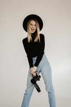 a woman in jeans and a black hat holding a camera with her right leg up