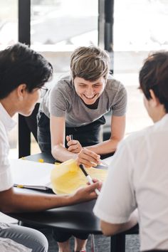 three people are sitting around a table and one person is writing on a piece of paper