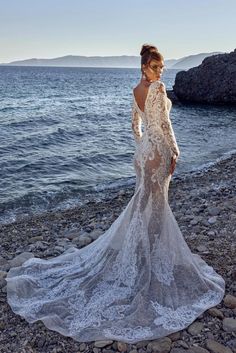 a woman standing on top of a rocky beach next to the ocean wearing a white dress